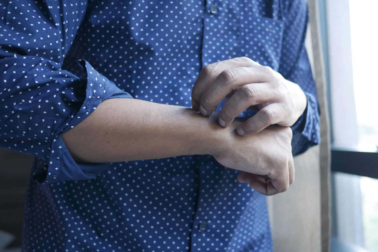 Person in a blue polka dot shirt scratching their forearm