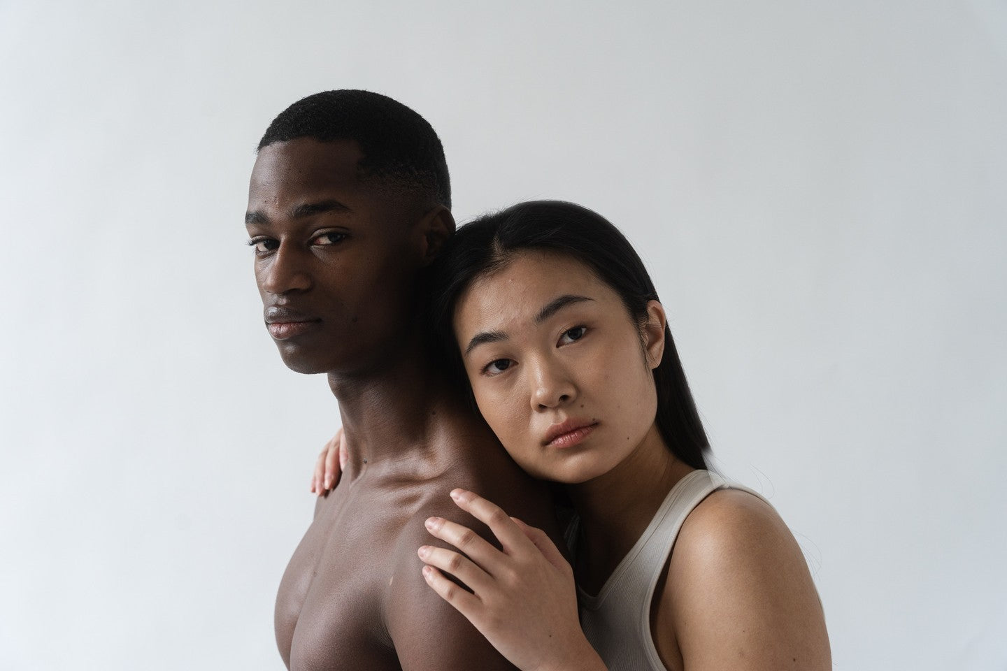 a man and woman standing close with her arms around his shoulders looking into the camera