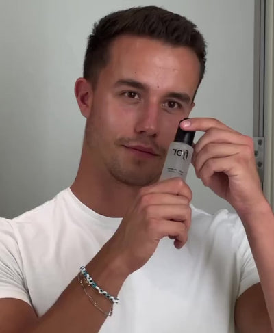 a man applying the fjör hydrolytic serum in the mirror in a white tshirt with a neutral background